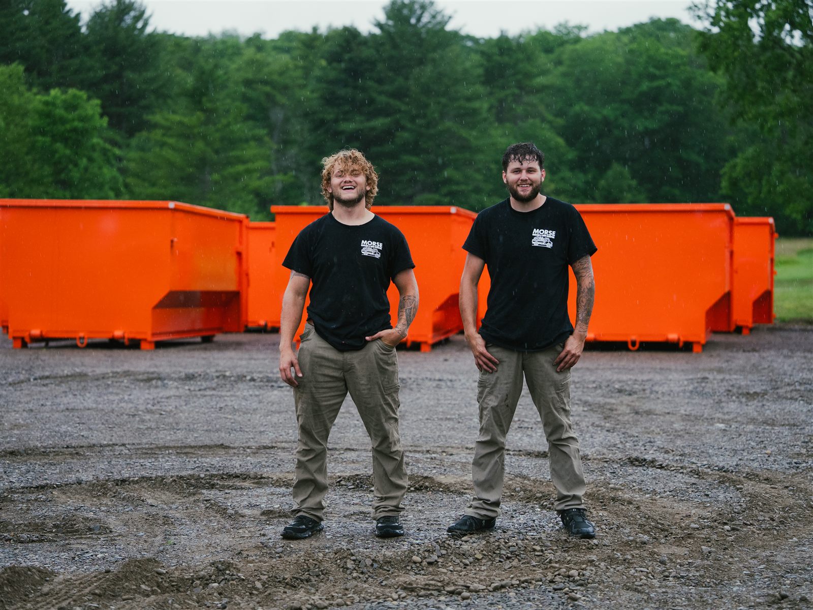 The Morse brothers standing in front of their orange roll-off dumpster fleet