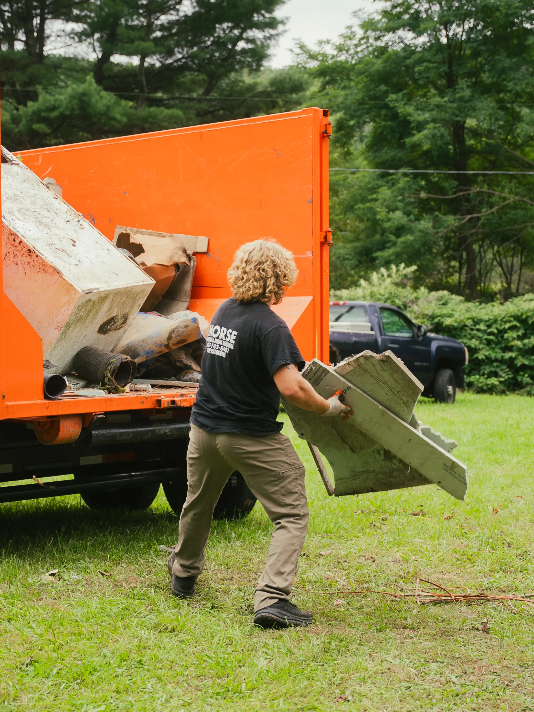 Morse Dumpsters crew member tossing debris into an orange roll-off dumpster, Corning NY
